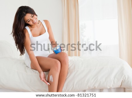 pretty woman putting creme on her legs while sitting on bed in bedroom