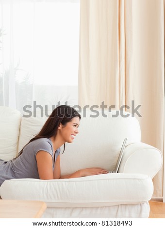 smiling woman lying on sofa with notebook in front of her in living room