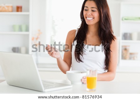 Pretty woman enjoying a bowl of cereal while relaxing with her laptop in the kitchen