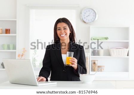 Gorgeous woman in suit relaxing with her laptop while holding a glass of orange juice in the kitchen