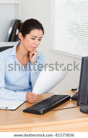 Beautiful woman looking at a computer screen while holding a sheet of paper at the office