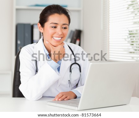 Attractive female doctor working with her laptop while sitting in her office