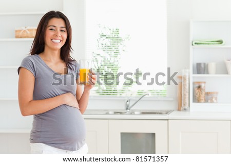 Charming pregnant woman holding a glass of orange juice while standing in the kitchen