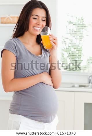 Attractive pregnant woman drinking a glass of orange juice while standing in the kitchen