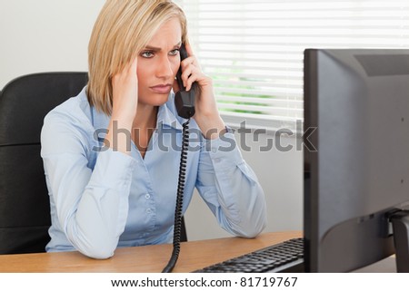 Blonde businesswoman on phone looking at screen while having headache in her office