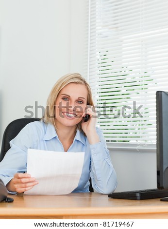 Portrait of a businesswoman looking up from a letter into camera while phoning in her office