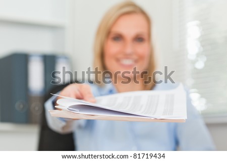 Smiling businesswoman passing a paper looks into camera in her office