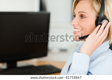 Portrait of a smiling blonde businesswoman with headset working with computer looking elsewhere in her office