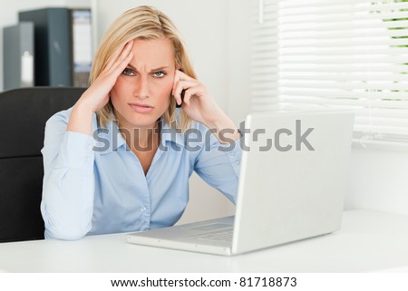 Frustrated blonde businesswoman on phone looks into camera in her office