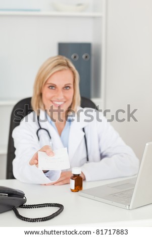Smiling doctor holding prescription looks into camera in her office