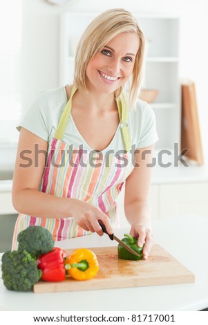 Gorgeous woman cutting green pepper looks into camera in kitchen
