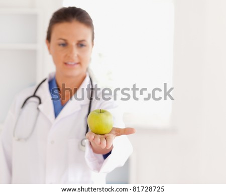 Good looking brunette doctor with stethoscope looking at an apple in the surgery