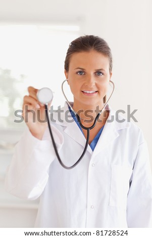 smiling brunette doctor presenting a stethoscope looking into the camera in her surgery