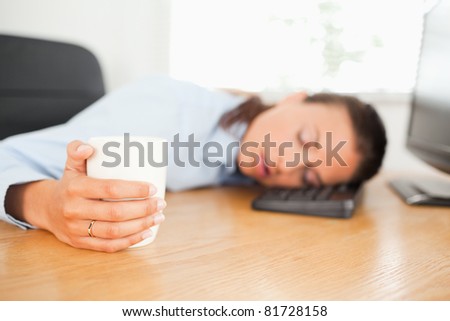 A sleeping businesswoman is holding a cup of coffee in an office