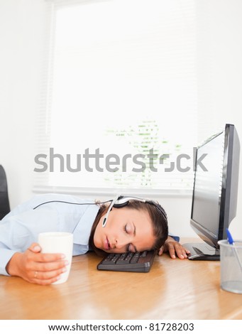 A secretary with a headset and a cup of coffee sleeps in an office