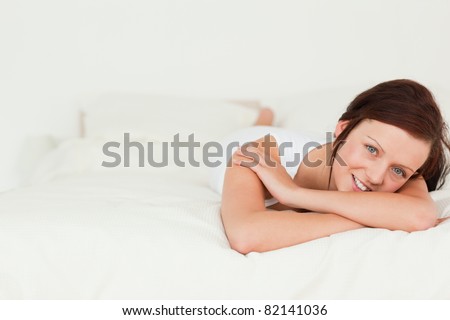 Red-haired woman relaxing on her bed looking into camera in her bedroom