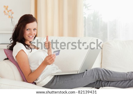 Woman with laptop and credit card holding thumb up in her living room