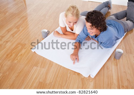 Young man showing a point on a plan to his fiance while lying on the floor