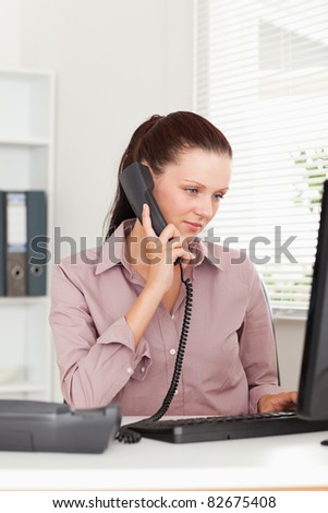 A focused businesswoman is telephoning and looking to the screen of her pc
