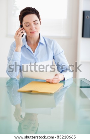 Businesswoman sitting behind a desk with papers on the phone in an office