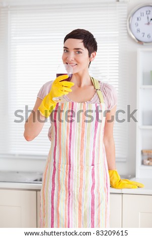 Smiling woman in cleaning gown with wine in a kitchen