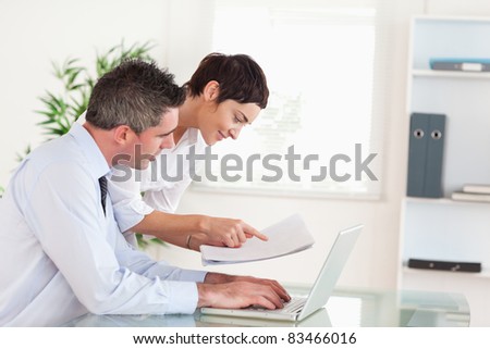 Coworkers comparing a blueprint folder to an electronic one in an office