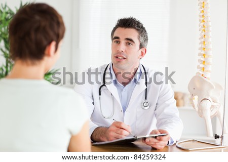 Male Doctor writing something down while patient is talking in a room