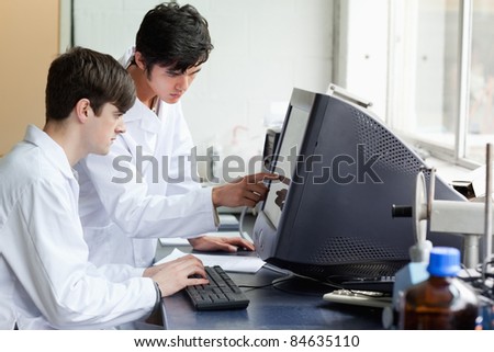 Chemist pointing at something on a monitor to his colleague in a laboratory