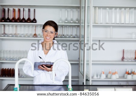 Smiling student in science writing on a clipboard in a laboratory