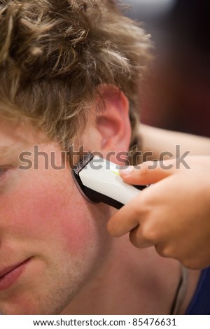 Portrait of a young man having a haircut with a hair clippers