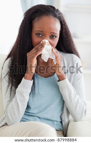 Close up of young woman on couch blowing her nose