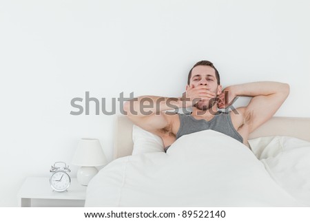 Tired man yawning while waking up in his bedroom