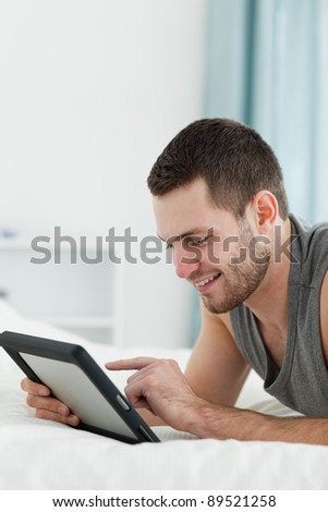 Portrait of a smiling man using a tablet computer while lying on his belly in his bedroom