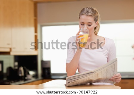 Young woman reading the news while drinking orange juice in her kitchen
