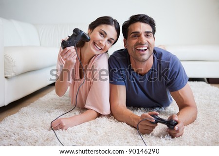 Delighted couple playing video games while lying on a carpet