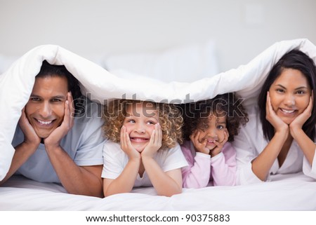 Smiling young family hiding under the blanket