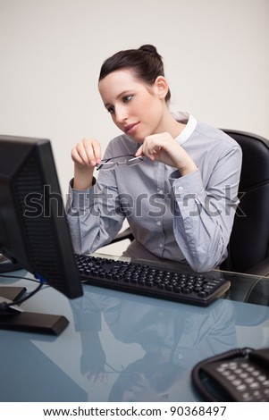 Young businesswoman looking at screen holding her glasses