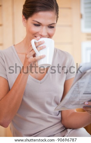Young woman taking a sip of coffee while reading newspaper