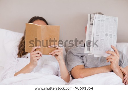 Woman reading a book while her companion is reading a newspaper in their bedroom