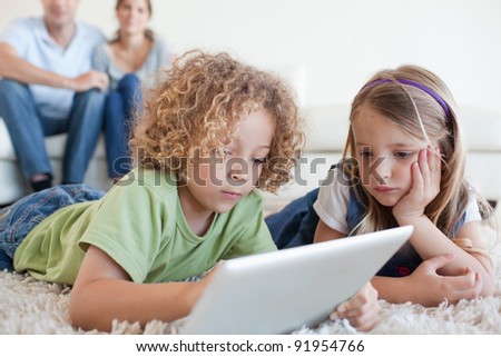Serious children using a tablet computer while their happy parents are watching in their living room