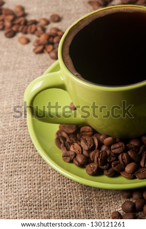Green cup of coffee with beans on background