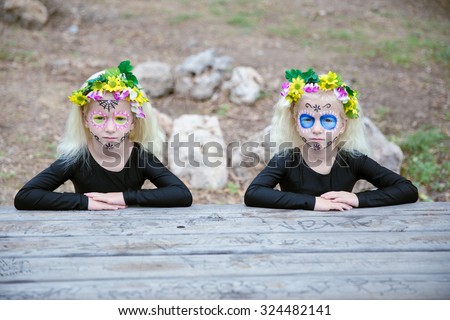 Photo of twin girls with black clothing and sugar skull makeup sitting in front of a table outdoors