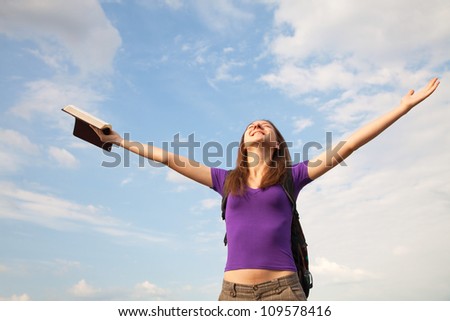 Young woman staying with raised hands against blue sky