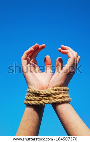 Hands tied up with rope against blue sky
