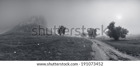 Surrealistic landscape with mountain peaks and sun in mist, in black and white
