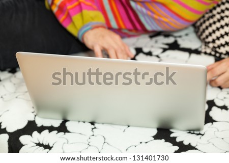 Woman in colorful blouse lying on black and white sofa and working on her laptop
