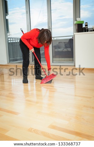 Middle aged housewife dusting wooden floor with red broom