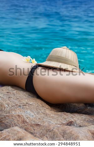 Woman lying on the beach with straw hat and frangipani flowers on her belly