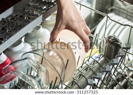 Close up of hand taking out clean dishes from dishwasher