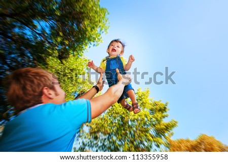 happy daddy is throwing  baby in a greenl summer park